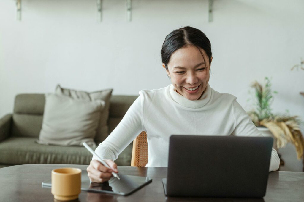 Woman smiling in front of her laptop while working on her business, illustrating the empowerment and success of female entrepreneurs."